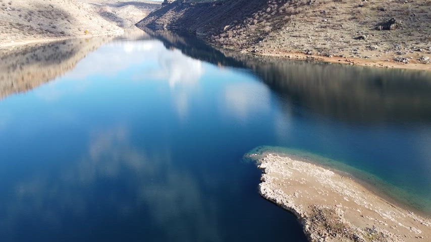 Kurak kayalık yamaçlar ile mavi baraj gölünün kontrastını gösteren sinematik drone görüntüsü. Renk geçişleri dikkat çekmektedir.