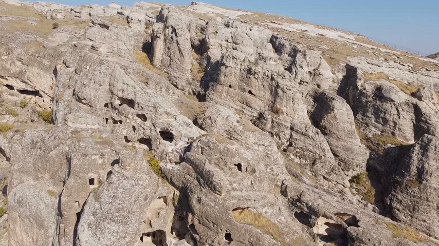 Kaya oyma odalar, mağara yerleşimleri ve dik kayalık yamaçlardan oluşan tarihî yerleşim alanı havadan panoramik açıyla görüntüleniyor. Arkeolojik doku, doğal kaya oluşumları ve kültürel miras özellikleriyle dikkat çeken bu manzara, Anadolu’nun tarihî yerleşim geleneğini yansıtıyor.