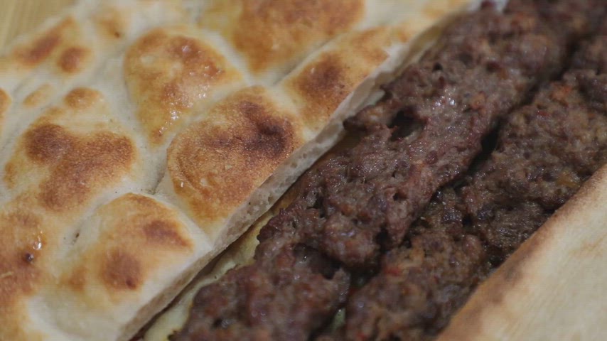 Izgara üzerinde pişirilmiş Adana kebap ve yanında servis edilen sıcak pide ekmeğinin yakın plan görüntüsü.