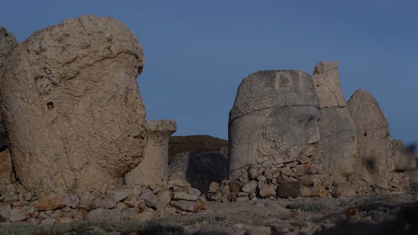 Nemrut Dağı'nın zirvesinde bulunan anıtsal taş heykel başlarını ve çevresindeki tarihi kalıntıları gösteren görüntü. Yüzyıllara meydan okuyan bu eserler, Anadolu'nun en etkileyici arkeolojik alanlarından birinde geçmişin izlerini günümüze taşıyor.