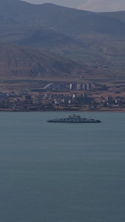 Van Gölü'nde seyreden feribot, kıyı yerleşimi ve dağ manzarasını bir araya getiren etkileyici drone görüntüsü.