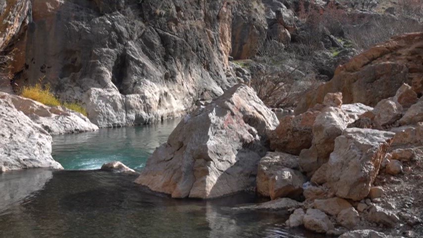 Sinek Çayı, drone kamerasından bakıldığında Çermik’in engebeli arazisi içinde parlayan bir şerit gibi görünüyor. Kayalık vadiler arasından kıvrılarak ilerleyen suyun masmavi rengi, çevredeki gri ve kahverengi dokuyla net bir kontrast oluşturarak bölgenin doğal yapısını tüm çıplaklığıyla sergiliyor.